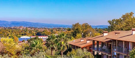 A villa with a terracotta roof, surrounded by lush greenery and a view of distant hills.
