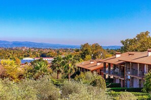 Una villa con techo de teja anaranjada, rodeada de vegetación exuberante y vistas a colinas distantes.
