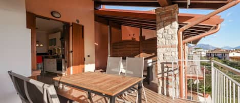 An outdoor dining area with a wooden table and chairs, a stone pillar, and a view of the mountains.