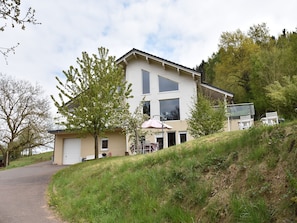 A two-story house with a garage, a patio with chairs, and a hill in the background. - Peaceful Getaway in Nature (VARSBERG)