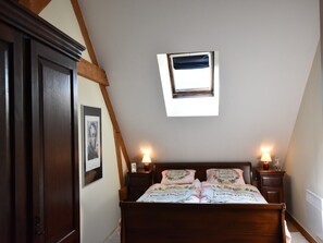 Een slaapkamer met een schuine hemel, dakraam, een bed met bloemenbedrukking, twee bedlampen en een ingelijst schilderij aan de muur.