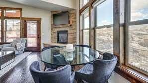 Una sala de estar moderna con una mesa de vidrio, sillas oscuras, una chimenea y amplios ventanales que ofrecen vistas del paisaje.