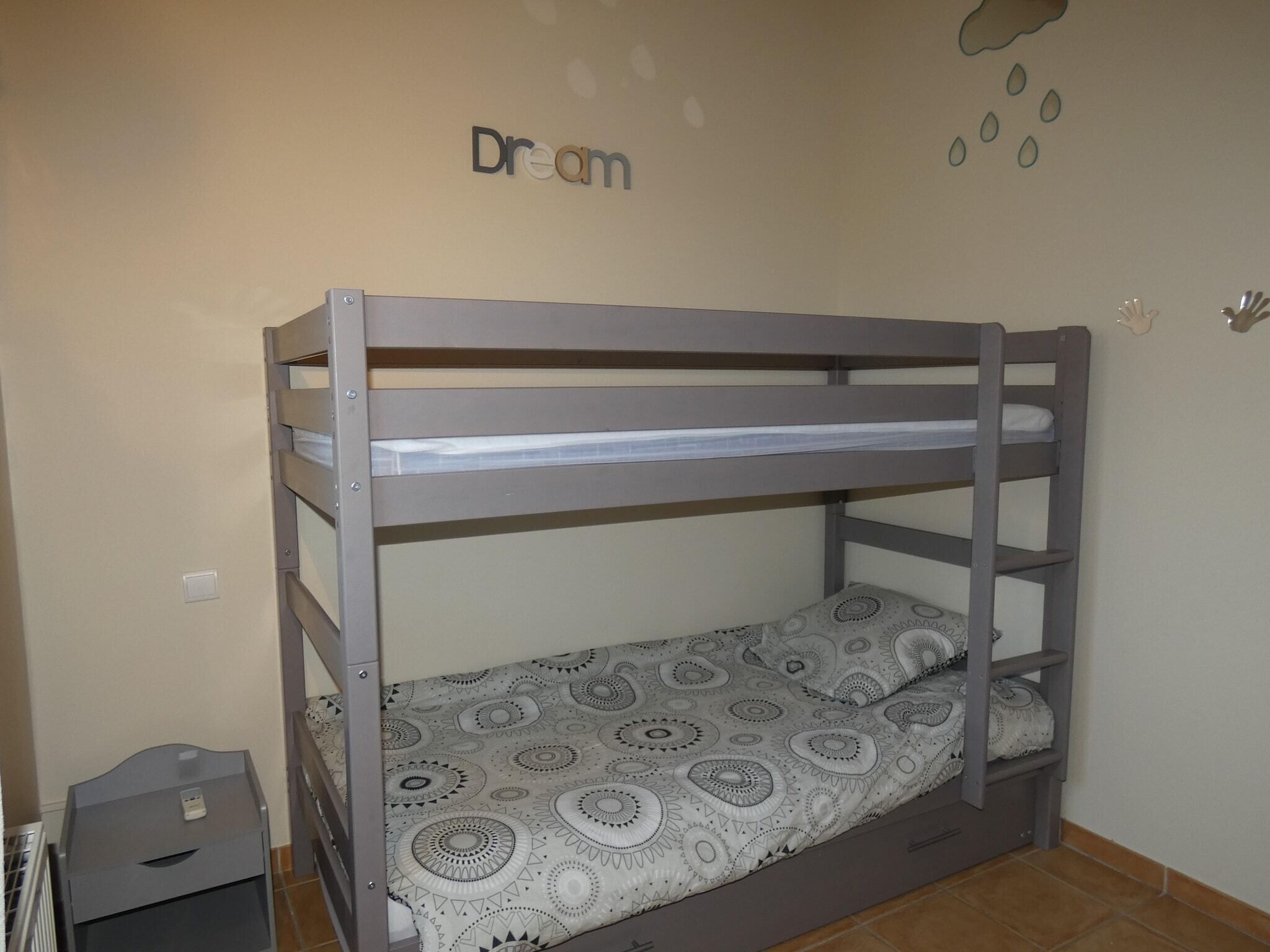 Un lit superposé avec un matelas à motifs dans une chambre décorée d’un autocollant mural représentant le mot « Rêve ».