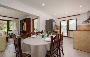 Ein Essbereich mit einem runden Tisch, gedeckt für vier Personen, umgeben von Holzstühlen. Es gibt eine Küchenzeile mit einer Arbeitsplatte und einem Kühlschrank.