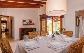 A dining room with a table set for six, wicker chairs, a wooden ceiling, and a large window.