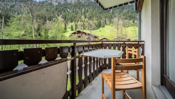 A balcony with a table and chair, overlooking a mountainous landscape with houses. - Apartment 'Les Avenières' with Balcony (Châtel)