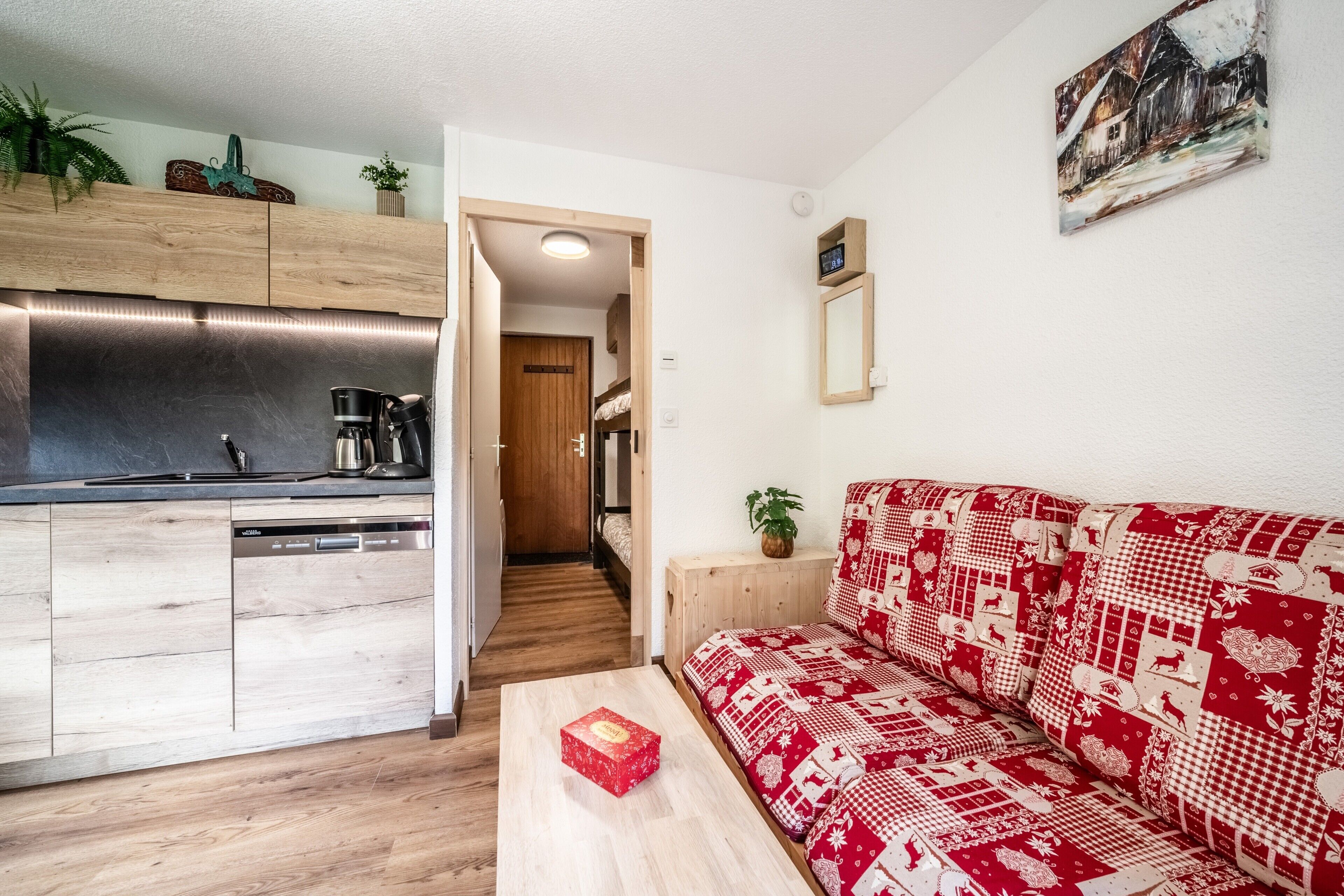 Une cuisine moderne avec des meubles en bois et un lave-vaisselle, un canapé rouge à motifs et une petite table avec une boîte.