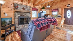 A cozy cabin interior with a stone fireplace, wooden walls, a television, and a dining area. - Bear Hugs cabin nestled in the woods. (Logan)
