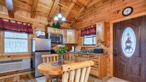 A wooden cabin interior with a kitchen, dining area, and a door with a decorative window. - Bear Hugs cabin nestled in the woods. (Logan)