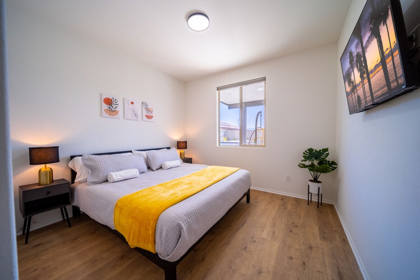 A bedroom with a bed, bedside lamps, a window, and a plant.