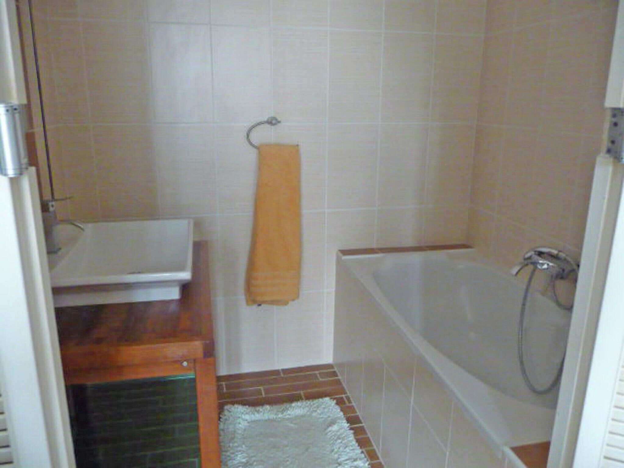 A bathroom with a white bathtub, a wooden shelf, and a white towel hanging on the wall.