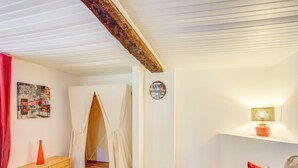 Una habitación acogedora con un banco de madera, una mesita, un sofá con cojines rojos, una lámpara de pared y una puerta que da a otra habitación.
