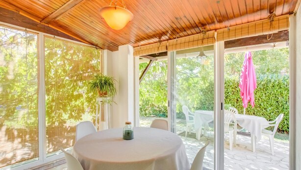 Una habitación iluminada por el sol con una mesa redonda, sillas y una planta colgante.