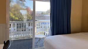 Ein Hotelzimmer mit Bett, kleinem runden Tisch, Stuhl und einem Balkon mit Geländer.