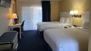 Ein Hotelzimmer mit zwei Betten, einem Schreibtisch mit Lampe, einem Sessel, einem an der Wand befestigten Fernseher und einem Fenster mit Vorhängen.
