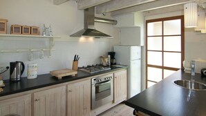 A kitchen with wooden cabinets, a gas stove, a refrigerator, and a window with blinds.