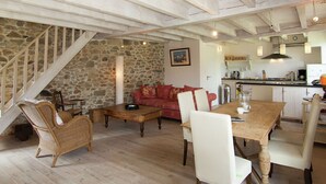 A cozy living room with a stone wall, a red sofa, wicker chairs, and a wooden dining table.