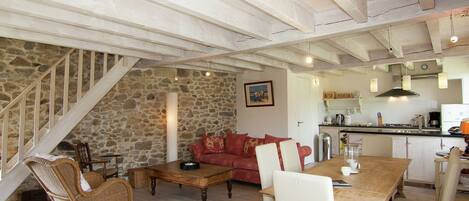 A cozy living room with a stone wall, a red sofa, wicker chairs, and a wooden dining table.