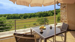 A table with a glass top and two chairs, an outdoor umbrella, and a scenic view of a green landscape with trees and a fence. - Romantic Tower in Dordogne with Rooftop Terrace (Roussines)