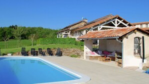 A poolside area with lounge chairs, a covered seating area, and a stone building with a tiled roof. - Romantic Tower in Dordogne with Rooftop Terrace (Roussines)