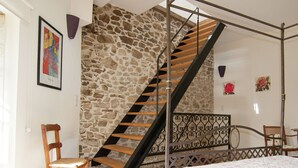 A bedroom with a stone wall, a wooden staircase, a bed, a chair, and a small table. - Romantic Tower in Dordogne with Rooftop Terrace (Roussines)