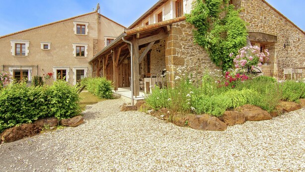 A stone building with a covered porch and a garden with flowers and shrubs. - Romantic Tower in Dordogne with Rooftop Terrace (Roussines)