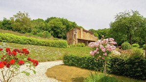 A garden with a gravel path, red roses, and a stone building. - Cottage in France with Covered Terrace (Roussines)