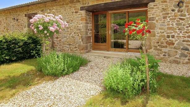 A stone building with a wooden door and windows, surrounded by gravel and greenery. - Cottage in France with Covered Terrace (Roussines)