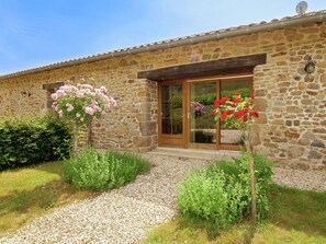 Un bâtiment en pierre avec une porte et des fenêtres en bois, entouré de gravier et de verdure.