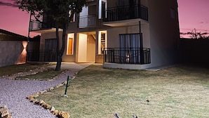 A modern two-story building with balconies, a tree in the front yard, and a clear sky. - Flat Aconchegante de Frente Para as Montanhas e Rodeado Pela Natureza (Alto Paraíso de Goiás)