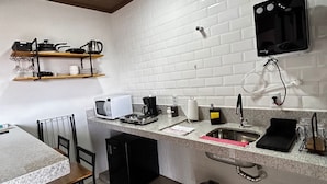 A compact kitchen with white brick walls, a built-in microwave, a coffee maker, and a small sink. - Flat Aconchegante de Frente Para as Montanhas e Rodeado Pela Natureza (Alto Paraíso de Goiás)