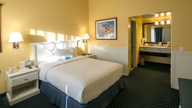 A hotel room with a large bed, bedside lamps, a nightstand, a framed picture on the wall, and a bathroom with a mirror and sink. - Cozy Standard Queen Room Near Beach and Across Lake! (Monterey)