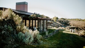A stone wall with a pergola and seating area, a stone chimney, and a grassy landscape with distant buildings. - Sagecliffe Resort & Spa (Quincy)