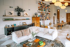 A spacious living room with a white sofa, a coffee table, and a bookshelf filled with photos.