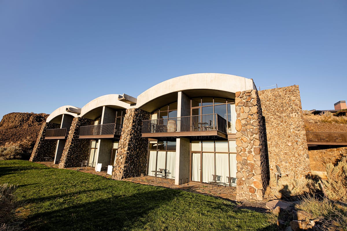 A modern building with curved architecture, stone walls, and a balcony with outdoor seating.