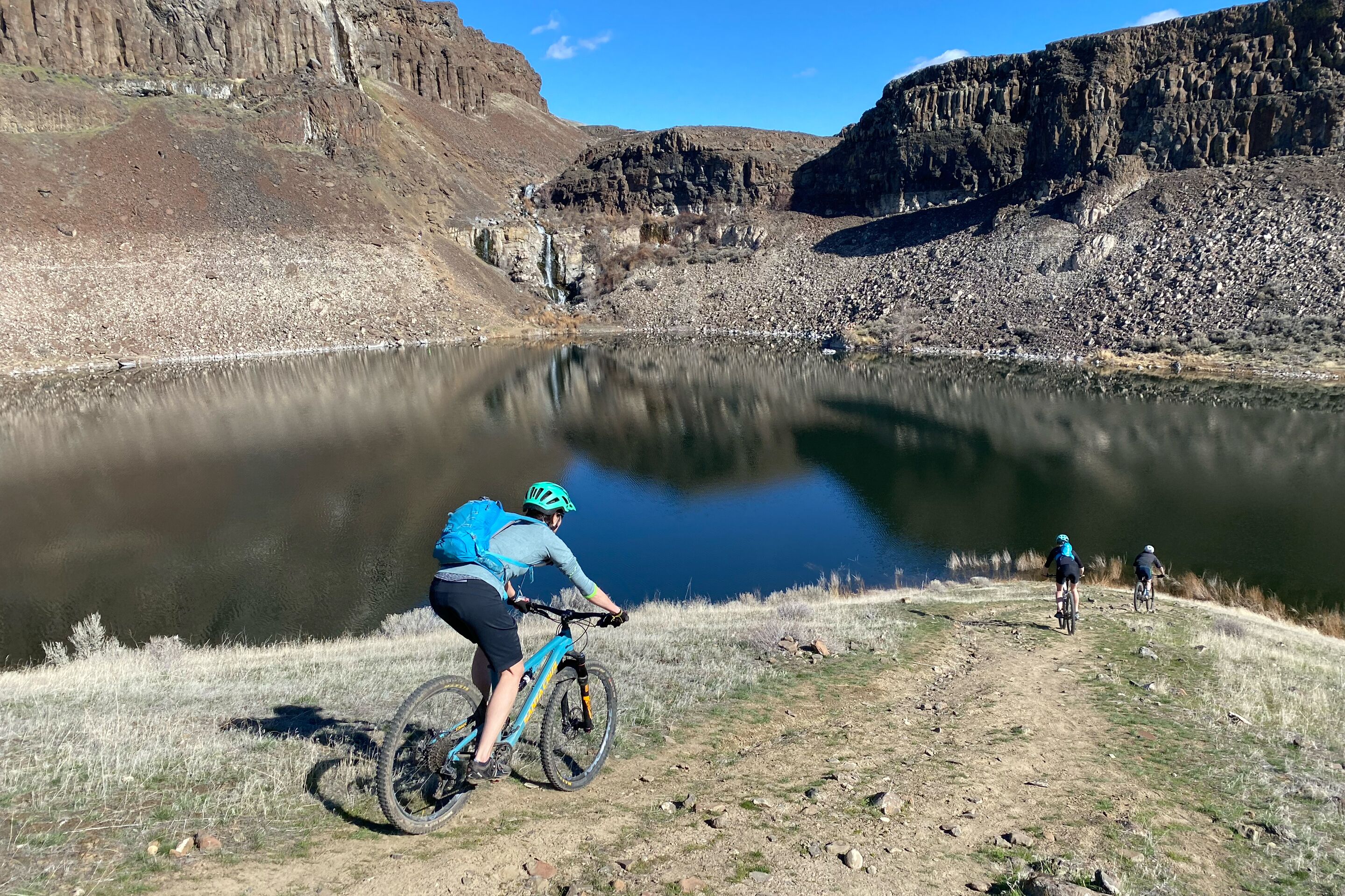 A mountain biking trail with a lake and rocky cliffs in the background.