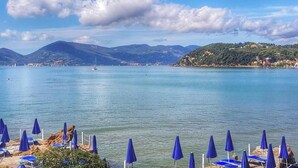 Une vue sur la côte, avec une eau cristalline, une plage parsemée de parasols bleus et une ville lointaine perchée sur une colline.