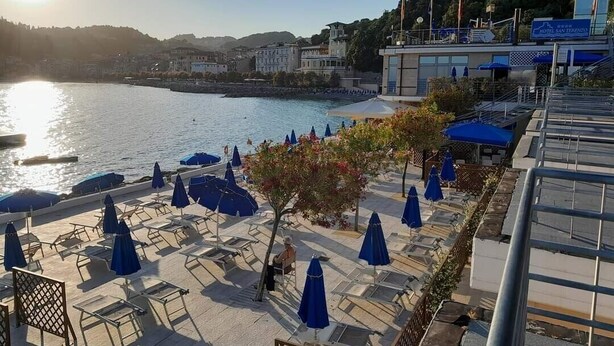 Un hôtel en bord de mer, doté d’une terrasse, offrant une vue sur l’eau et dont le bâtiment est reconnaissable grâce à une enseigne.