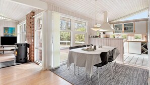 A modern kitchen with white cabinets, a dining area with a table and chairs, and a large window providing a view of the outdoors.