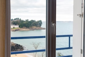 A coastal view from a balcony with a railing, a building on the shore, and calm waters. - Sea View Apartment 'Face Mer - 50m Beach' (Douarnenez)