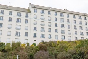 Un hotel de varios pisos con balcones, techo plano y un área de jardín densa en primer plano.