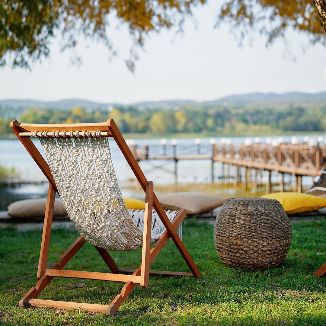 A hammock chair with a woven seat and backrest, wooden frame, and a round woven ottoman beside it.