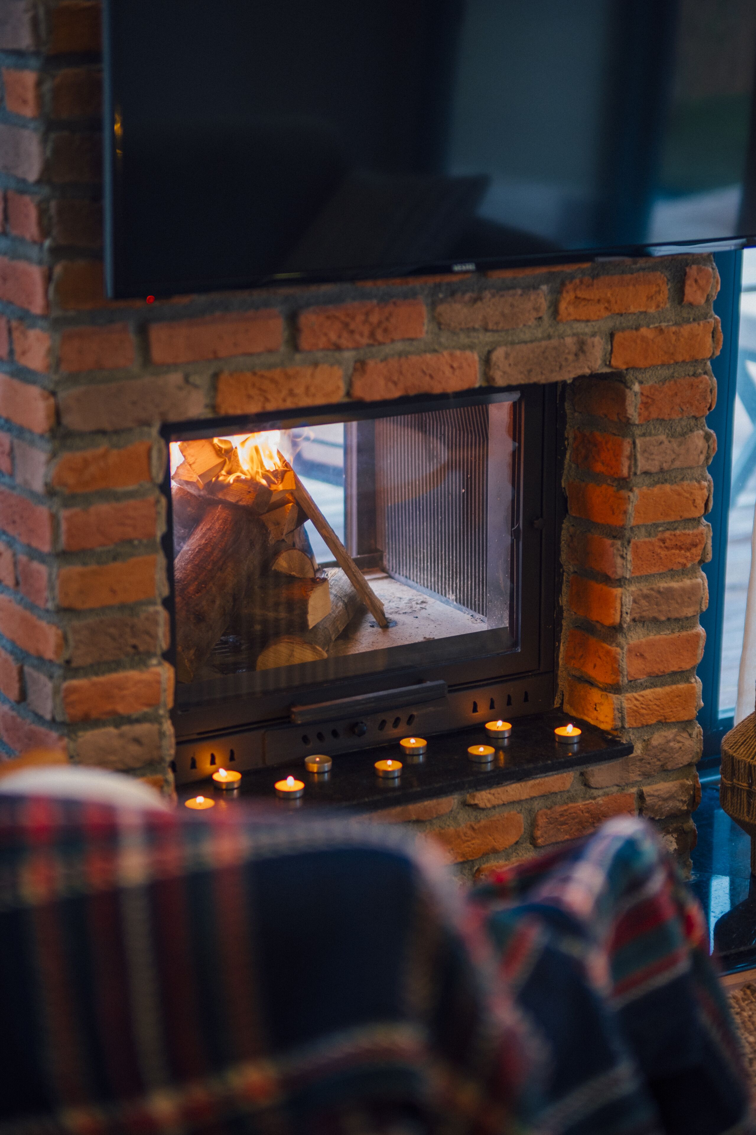 A fireplace with a TV mounted above it, a fire burning inside, and candles on the mantel.