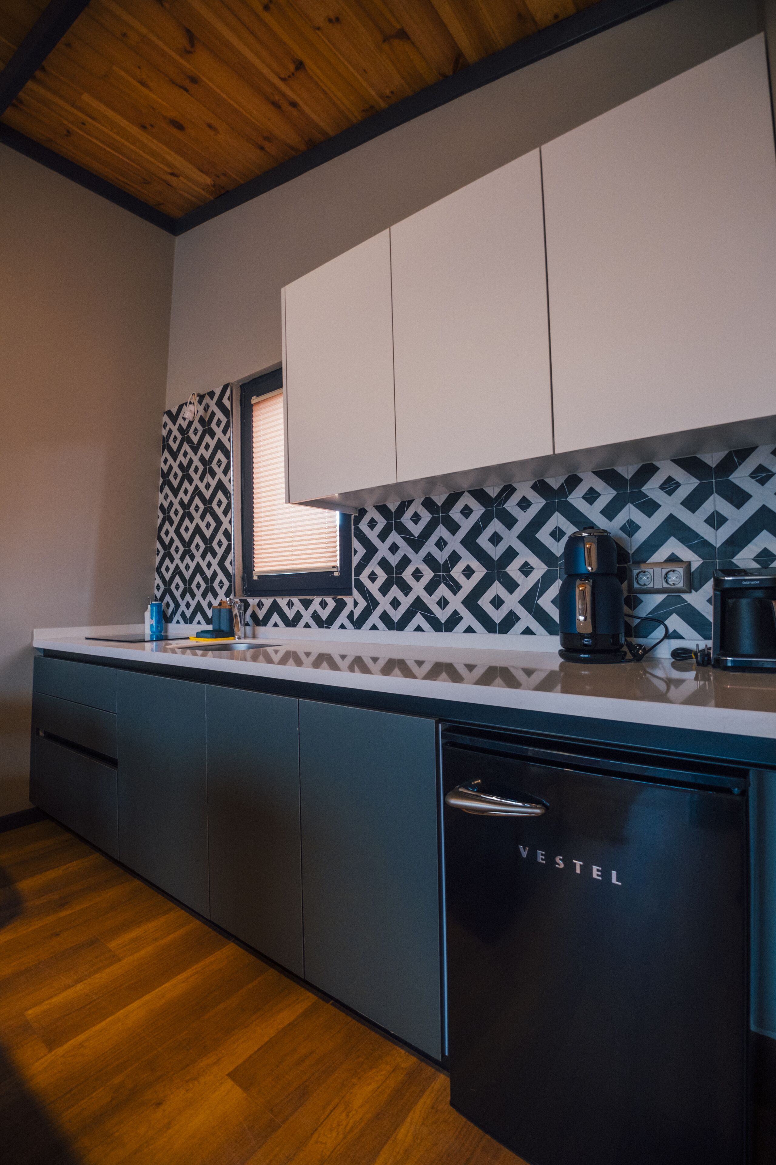 A modern kitchen with a wooden ceiling, patterned backsplash, and a black refrigerator labeled 'VESTEL'.