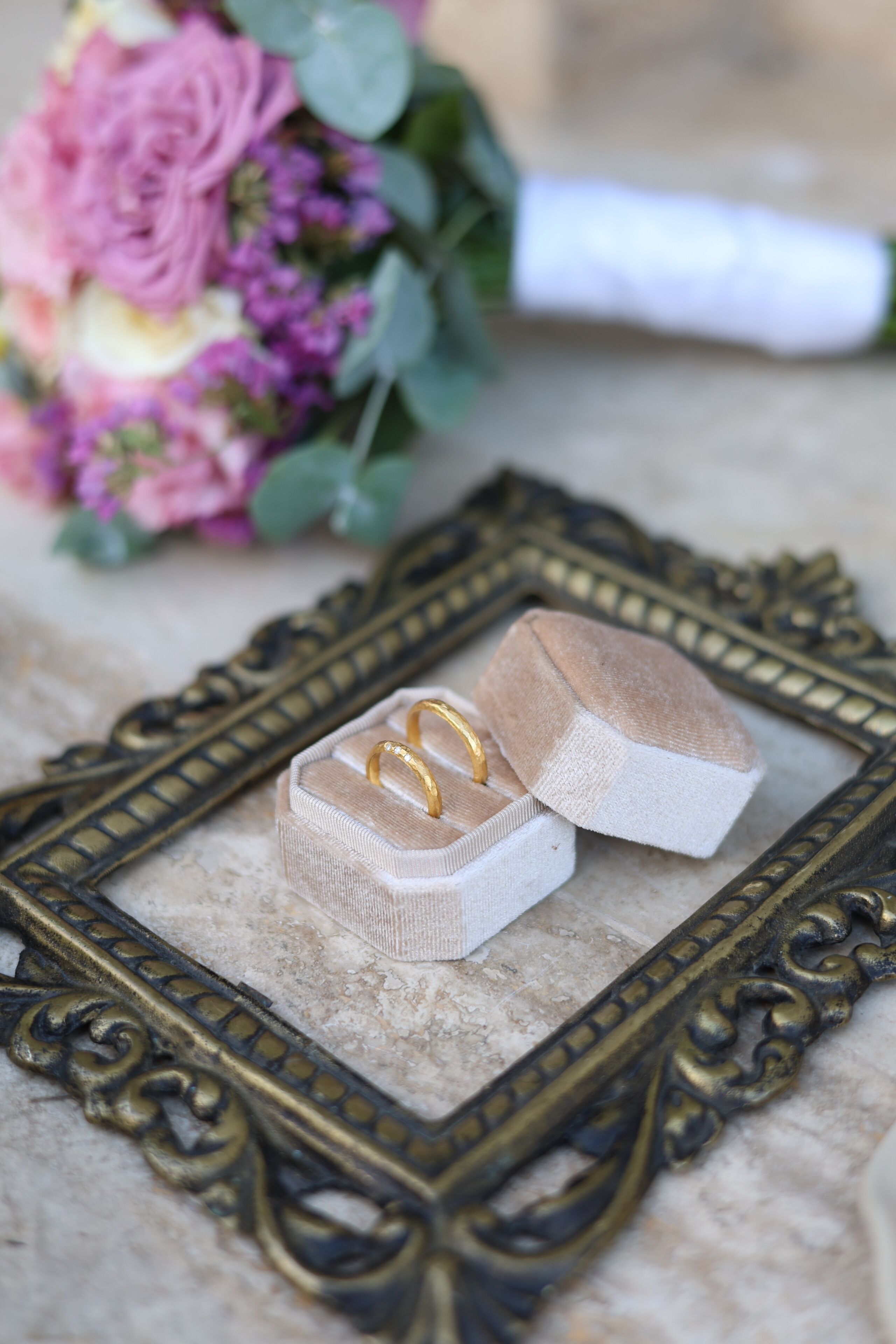 A hexagonal jewelry box with two gold rings on a marble surface, surrounded by a decorative frame.