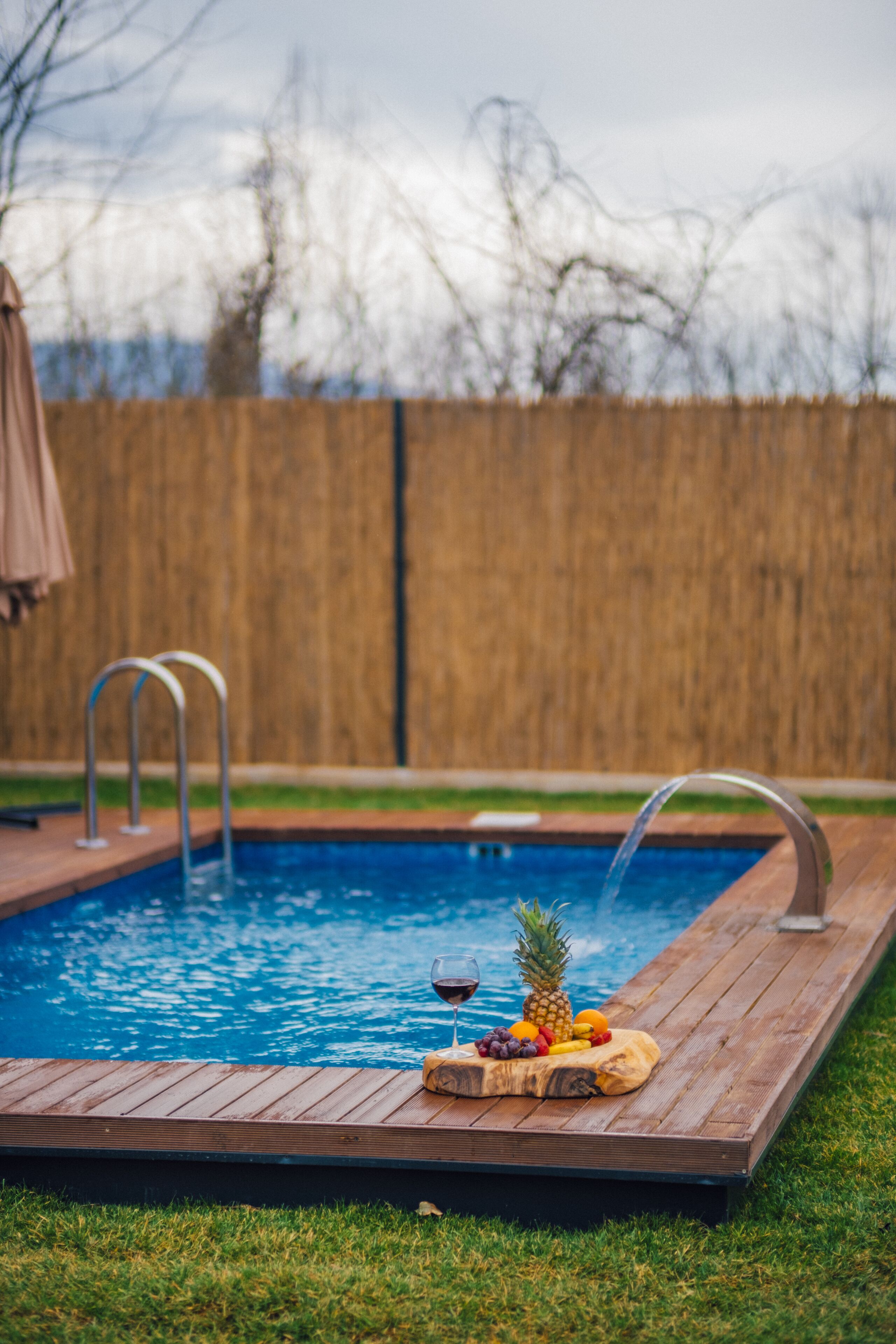 Una piscina con cubierta de madera, una presentación de bebidas y fruta, y una valla de madera al fondo.