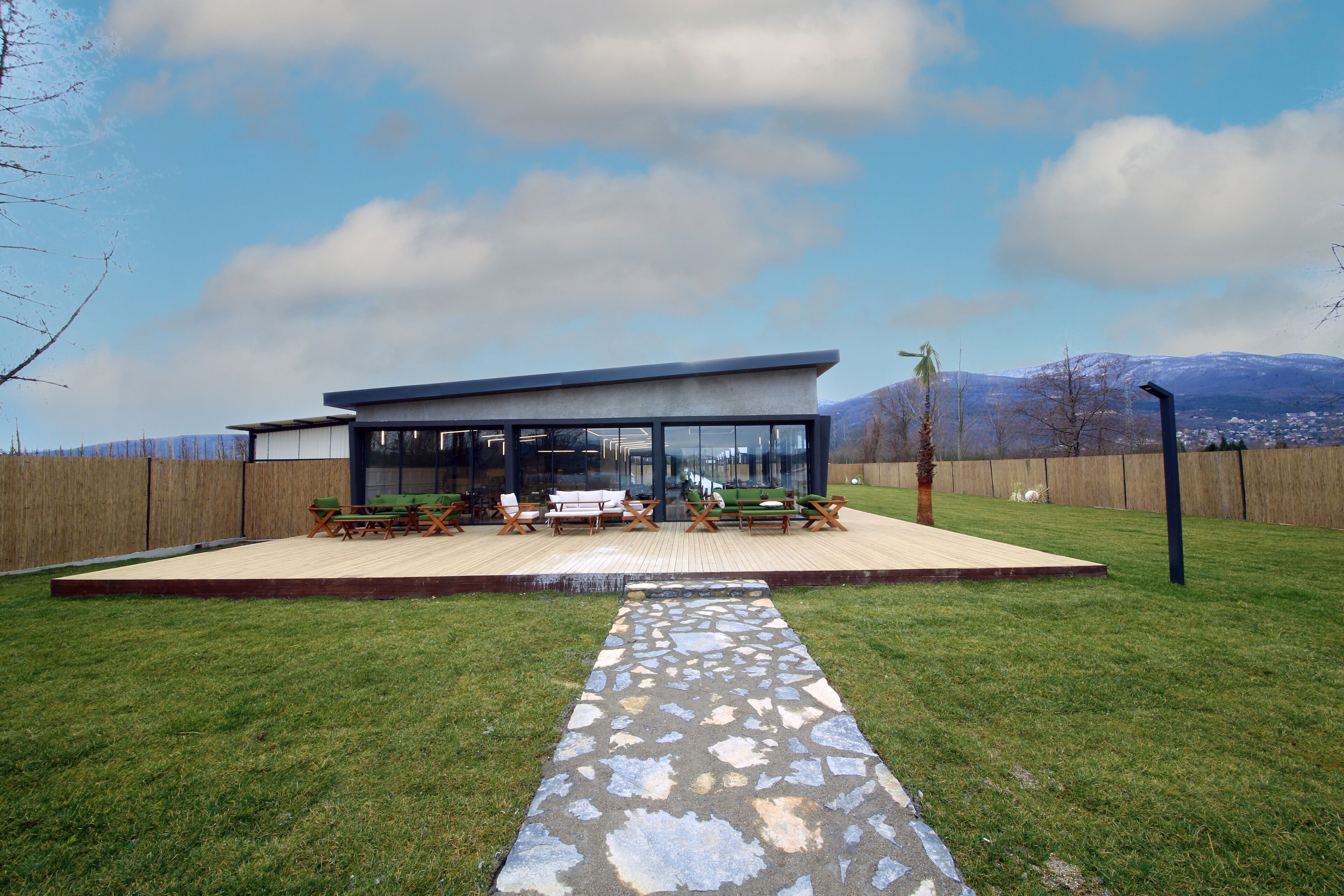 A modern house with a patio area, a stone pathway, and a view of mountains in the background.