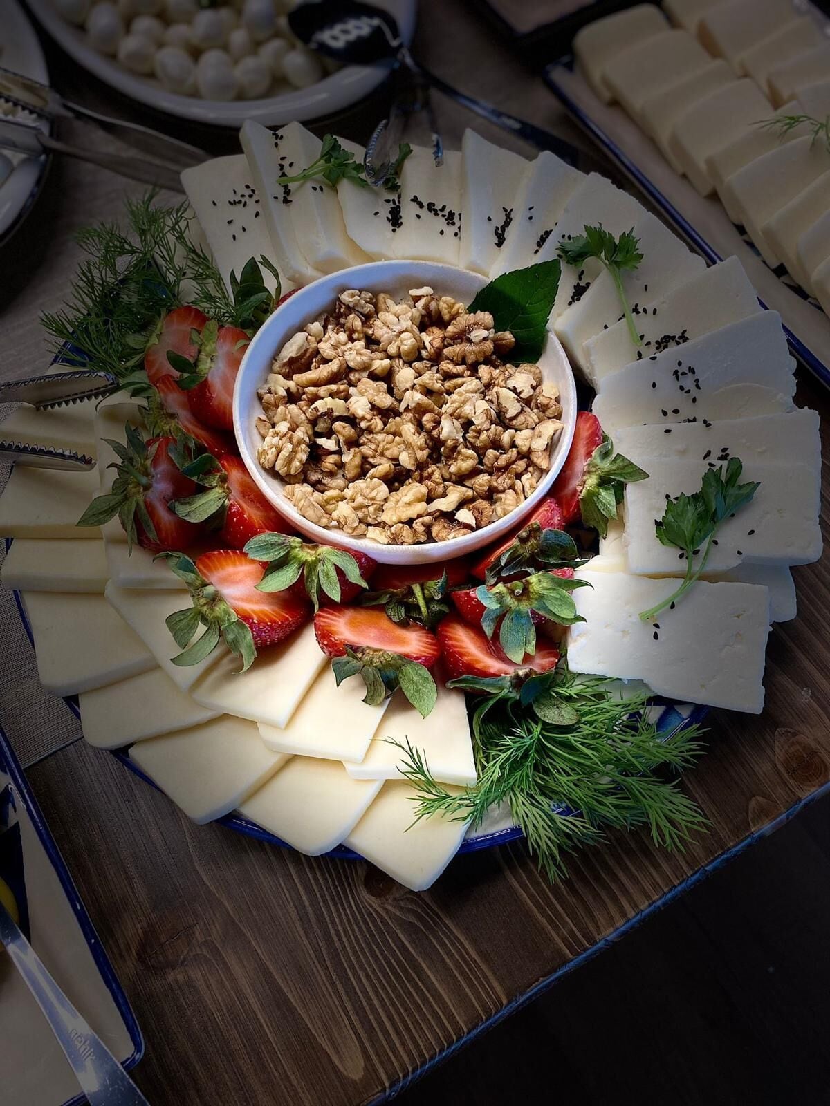 A platter of assorted cheeses, strawberries, and walnuts arranged on a wooden table.