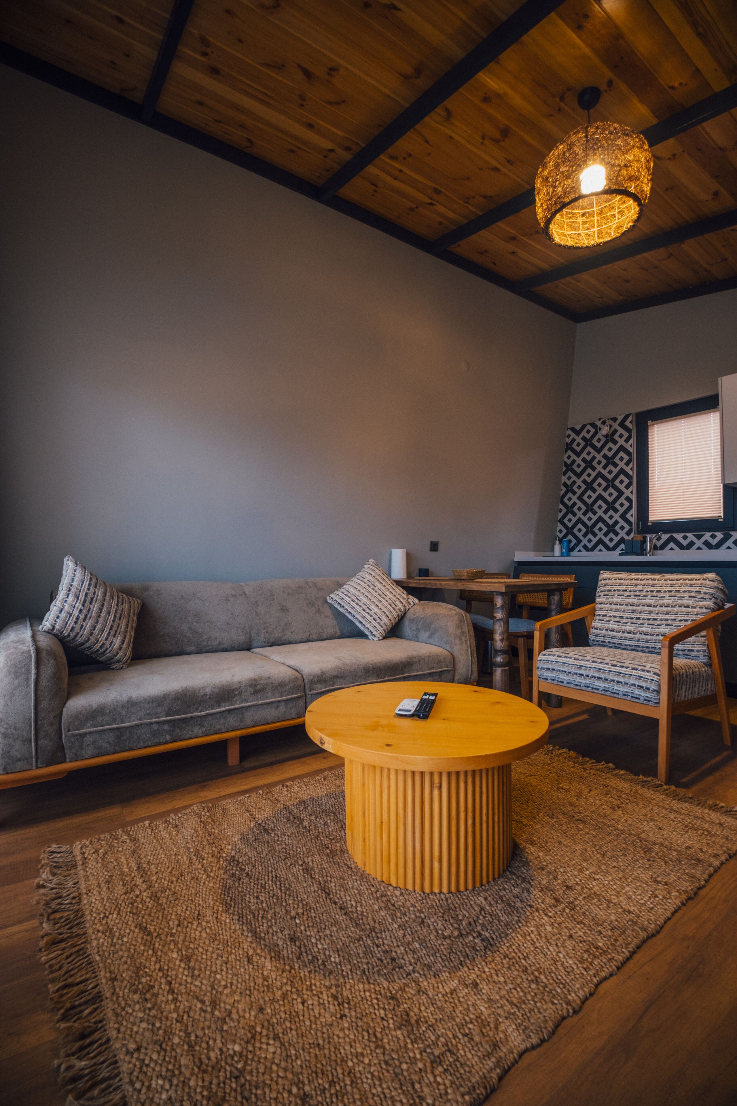 Una habitación acogedora con un sofá gris, una mesa de centro de madera y una pared con estampado.
