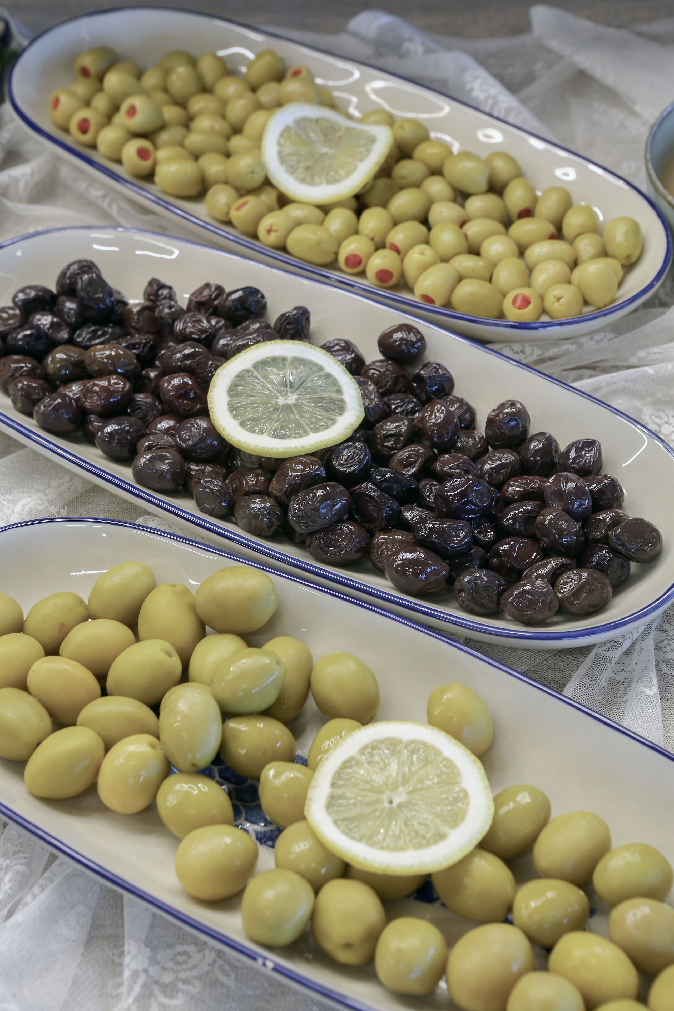 Three oval-shaped dishes containing olives, some with lemon slices.